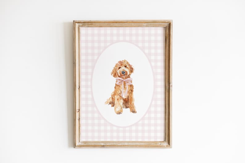May include: A framed print of a watercolor painting of a golden doodle dog wearing a pink bow, set against a pink and white gingham background.