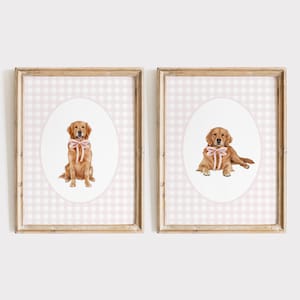 May include: Two framed prints featuring watercolor illustrations of Golden Retrievers. Each dog wears a pink bow. The background is a pink and white gingham pattern. The frames are a light wood color. One dog is sitting, the other is lying down.