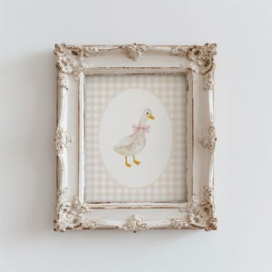 May include: A white framed print with a gingham background and a white duck with a pink bow in a circular frame.