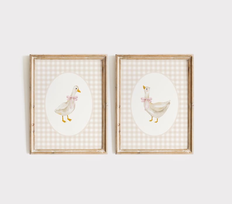 May include: Two framed prints with a beige and white gingham background. Each print features a white duck with a pink bow on a white oval.