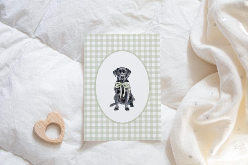 May include: A black Labrador Retriever wearing a green bow tie sits in a white oval on a green and white gingham background.