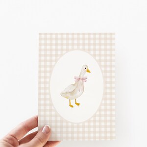 May include: A white goose with a pink bow is illustrated on a beige and white gingham background. The goose is standing on a white oval.