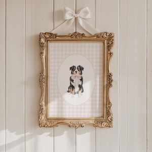 May include: A framed dog portrait with a gold ornate frame and a white bow. The artwork features a dog with black, white, and brown fur, wearing a pink bow tie, set against a pink gingham background.