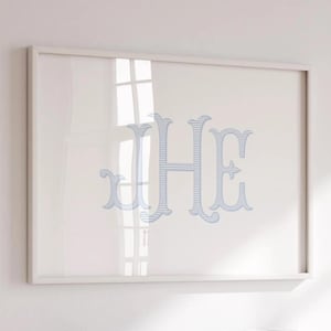 May include: Framed artwork featuring the letters "JHE" in a light blue, striped design. The letters are large and ornate, set against a white background. The frame is a simple, light color, and the artwork is displayed on a white wall.