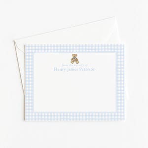 May include: A stationery set featuring a light blue gingham pattern border. The card has a teddy bear illustration and the text "from the nursery of Henry James Peterson". An envelope is included.