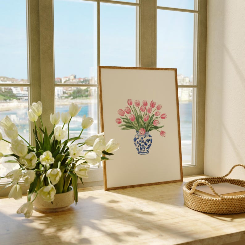 May include: A framed print of a bouquet of pink tulips in a blue and white porcelain vase. The vase has a floral design. The print is on a white background and has a wooden frame.