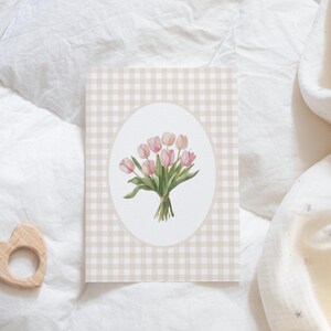 Pu&ograve; includere: Una carta con un motivo a quadri vichy presenta un bouquet di tulipes rosa e verdi in una cornice ovale bianca.