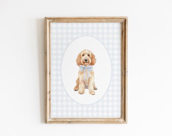 May include: A framed watercolor print of a golden-colored dog with a blue bow tie. The dog is centered on a white oval against a light blue and white gingham pattern. The frame is a light brown color.
