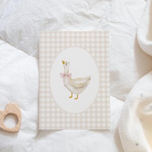 May include: A white goose with a pink bow on a beige and white gingham background.