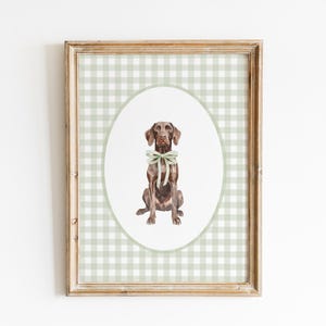 Peut inclure: Une impression encadrée représentant une illustration à l'aquarelle d'un chien marron avec un nœud vert. Le chien est centré sur un ovale sur un fond vichy vert clair. Le cadre est de couleur marron clair.