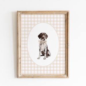 May include: A framed print of a brown and white German Shorthaired Pointer dog wearing a beige bow tie, sitting on a beige and white gingham background.