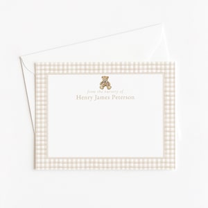 May include: A personalized stationery set featuring a cream-colored envelope and a matching card. The card has a beige gingham border and a small teddy bear illustration. The text "from the nursery of Henry James Peterson" is printed in a delicate font.