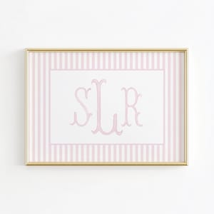 May include: A framed print featuring a pink monogram on a white background, surrounded by a pink and white striped border. The frame is gold. The monogram appears to be the letters S, L, and R.