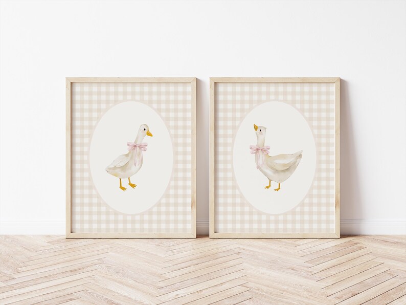 May include: Two framed prints of watercolor illustrations of white ducks with pink bows on a beige gingham background.