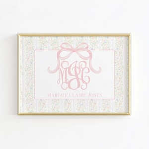 May include: A rectangular wall art print in a gold frame featuring a white centre panel with a pink watercolour bow and the monogram MCJ above the text MARGOT CLAIRE JONES. The border has a vertical striped pattern with small floral motifs.