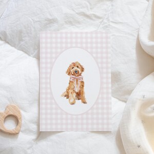 May include: A pink and white gingham card with a white oval in the center. Inside the oval is a watercolor illustration of a brown and white dog wearing a pink bow.