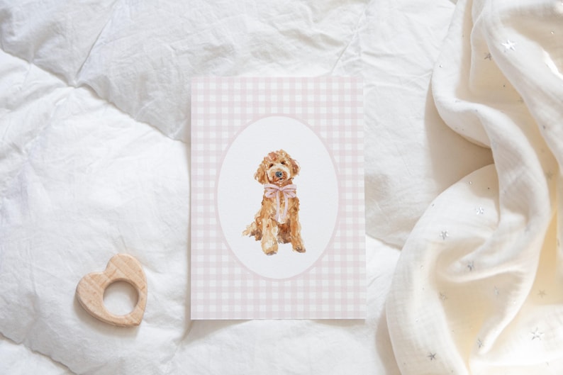 May include: A pink and white gingham card with a white oval in the center. Inside the oval is a watercolor illustration of a brown and white dog wearing a pink bow.