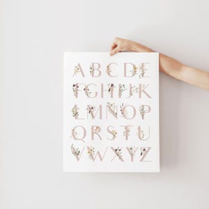 May include: A white poster with a floral alphabet printed in pink. The letters are surrounded by watercolor flowers and leaves.