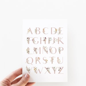 May include: A white card with the alphabet printed in pink letters. Each letter is decorated with a floral design in shades of pink, yellow, and brown.