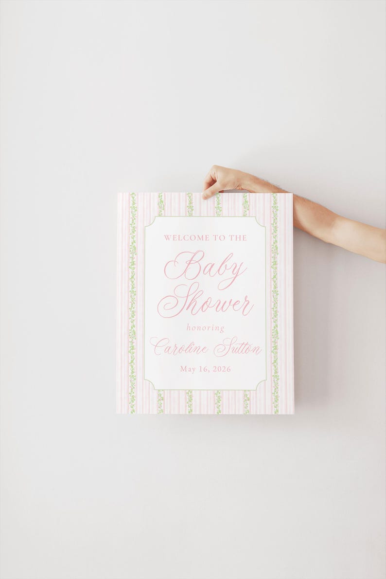 May include: A baby shower sign with a pink and white striped pattern and green floral borders. The sign displays the text "Welcome to the Baby Shower honoring Caroline Sutton May 16, 2026" in a decorative font.