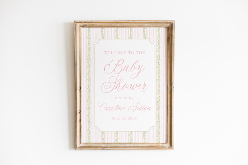 May include: A framed baby shower announcement. The sign has a pink and white striped background with a decorative border. The text reads "Welcome to the Baby Shower honoring Caroline Sutton May 16, 2026."