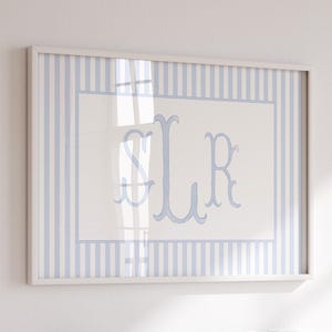 May include: Framed artwork featuring a light blue and white striped border. The center displays a white background with light blue monogram letters "SLR". The artwork is encased in a white frame, suitable for home decor.