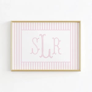 May include: A framed print featuring a pink and white striped background with a white center. The center displays a pink monogram in a delicate script font. The frame is gold.