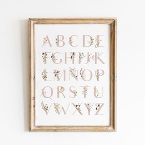 May include: A framed print of the alphabet with each letter decorated with floral illustrations in shades of pink, yellow, and white.