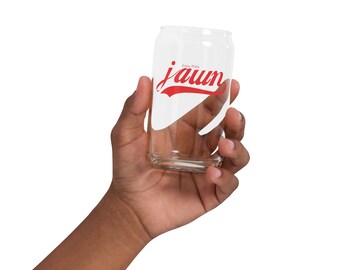 May include: A clear glass can with a red "jaun" logo and the text "Enjoy Philly" printed on it. The can is being held by a hand.