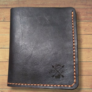 May include: Black leather wallet with orange stitching and a small logo embossed on the front. The logo features a cross with arrows and the letters "O+H".