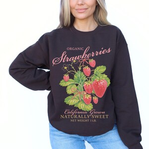 May include: Dark brown sweatshirt with a vintage-style strawberry graphic. The graphic includes the word "Organic" above the word "Strawberries" in pink script, and the words "California Grown, Naturally Sweet" below the strawberry illustration. Net weight is 1 lb.