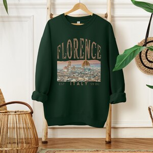 May include: A dark green sweatshirt with a vintage-style graphic of the Florence skyline and the text "FLORENCE EST. ITALY 59 BC".