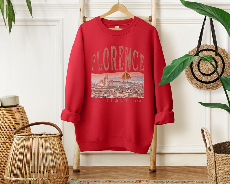 May include: Red sweatshirt with a graphic print of the Florence skyline and the text "FLORENCE EST. ITALY 59 BC".