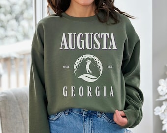 May include: A green sweatshirt with the text "AUGUSTA SINCE 1932 GEORGIA" and a white silhouette of a golfer in a circle with golf balls.