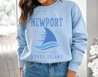 May include: Light blue sweatshirt with the text "NEWPORT SAILING CLUB RHODE ISLAND" and a blue sailboat graphic.
