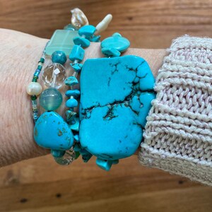 May include: A stack of turquoise and green gemstone bracelets with a large turquoise stone in the centre.