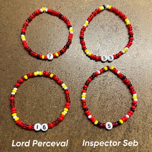 K&ouml;nnte beinhalten: Vier Perlenarmb&auml;nder mit roten, gelben, wei&szlig;en und schwarzen Perlen. Jedes Armband hat eine wei&szlig;e Perle mit einer Nummer darauf. Die Armb&auml;nder sind mit "Iceman", "Smooth Operator", "Lord Perceval" und "Inspector Seb" beschriftet.