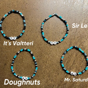 K&ouml;nnte beinhalten: Vier Perlenarmb&auml;nder mit verschiedenen Perlenfarben und Zahlen. Die Armb&auml;nder sind mit "It's Valtteri", "Sir Lewis", "Doughnuts" und "Mr. Saturday" beschriftet.