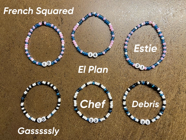 K&ouml;nnte beinhalten: Sechs Perlenarmb&auml;nder mit verschiedenen Farbkombinationen und Namen auf den Anh&auml;ngern. Die Namen sind "French Squared", "El Plan", "Estie", "Gasssssly", "Chef" und "Debris".