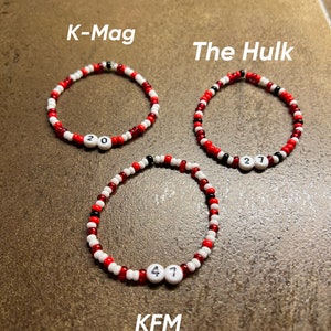 K&ouml;nnte beinhalten: Drei rote, wei&szlig;e und schwarze Perlenarmb&auml;nder mit wei&szlig;en Buchstabenperlen, die "K-Mag 20", "The Hulk 27" und "KFM 47" buchstabieren.