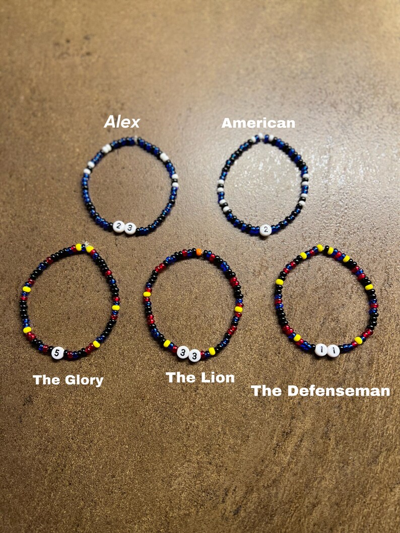 K&ouml;nnte beinhalten: F&uuml;nf Perlenarmb&auml;nder mit verschiedenen Farbkombinationen und Zahlen. Die Armb&auml;nder sind mit "Alex", "American", "The Glory", "The Lion" und "The Defenseman" beschriftet.