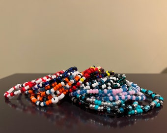 May include: A pile of colorful beaded bracelets in various colors, including red, blue, black, white, orange, pink, turquoise, and silver.
