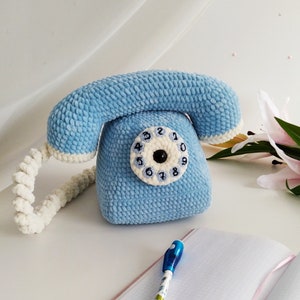 May include: A blue crocheted plush toy telephone with a white cord and a white dial with black numbers.