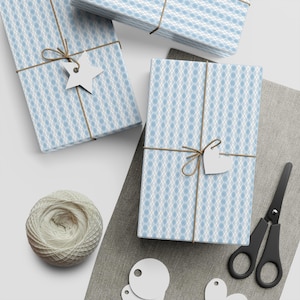Könnte beinhalten: Drei Geschenkboxen, die in blau-weiß gemustertes Papier mit Schnur und Etiketten verpackt sind. Die Boxen befinden sich auf einer weißen Oberfläche mit einer braunen Stoffoberfläche im Hintergrund.