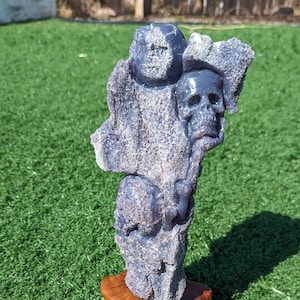 May include: A purple amethyst skull sculpture on a wooden base. The sculpture is carved in the shape of a tree with multiple skulls and orbs.