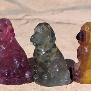 Op de afbeelding: Drie gegraveerde fluoritehondjes. Het hondje links is paars, het middelste hondje is grijs en groen, en het hondje rechts is geel en oranje.
