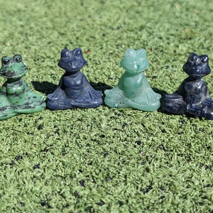 Puede incluir: Cuatro pequeñas figuritas de rana verde y azul en posición de meditación. Las ranas están hechas de piedra pulida y tienen ojos negros.