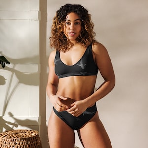 May include: A black two-piece swimsuit with a shark print. The top is a scoop neck with a racerback style. The bottom is a high-waisted bikini bottom.