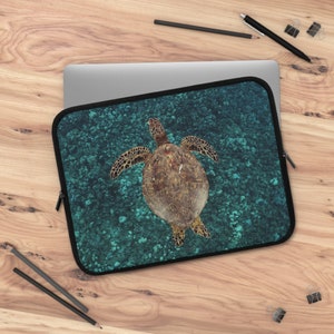 May include: A laptop sleeve with a green and blue design featuring a sea turtle swimming in the ocean.