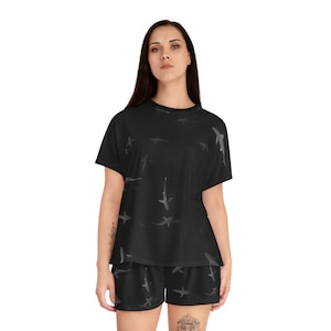 May include: Black pajama set with a short-sleeved shirt and shorts. The shirt and shorts feature a repeating pattern of gray sharks.